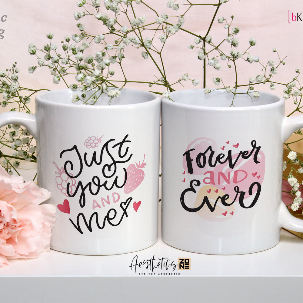 Two white mugs with romantic text design on a decorative background with flowers and gift boxes.