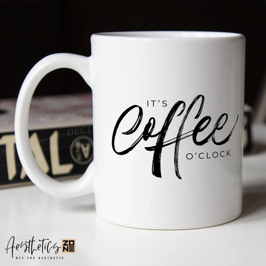 White coffee mug with 'It's Coffee O'Clock' text on a blurred background