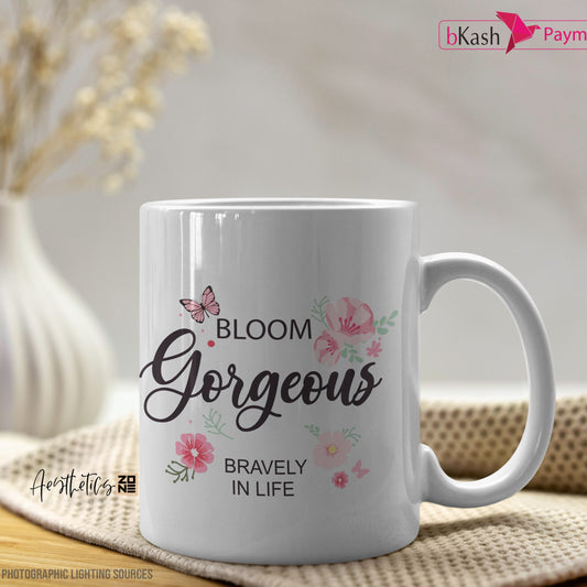 White mug with 'Bloom Gorgeous Bravely in Life' text and floral designs on a wooden surface.