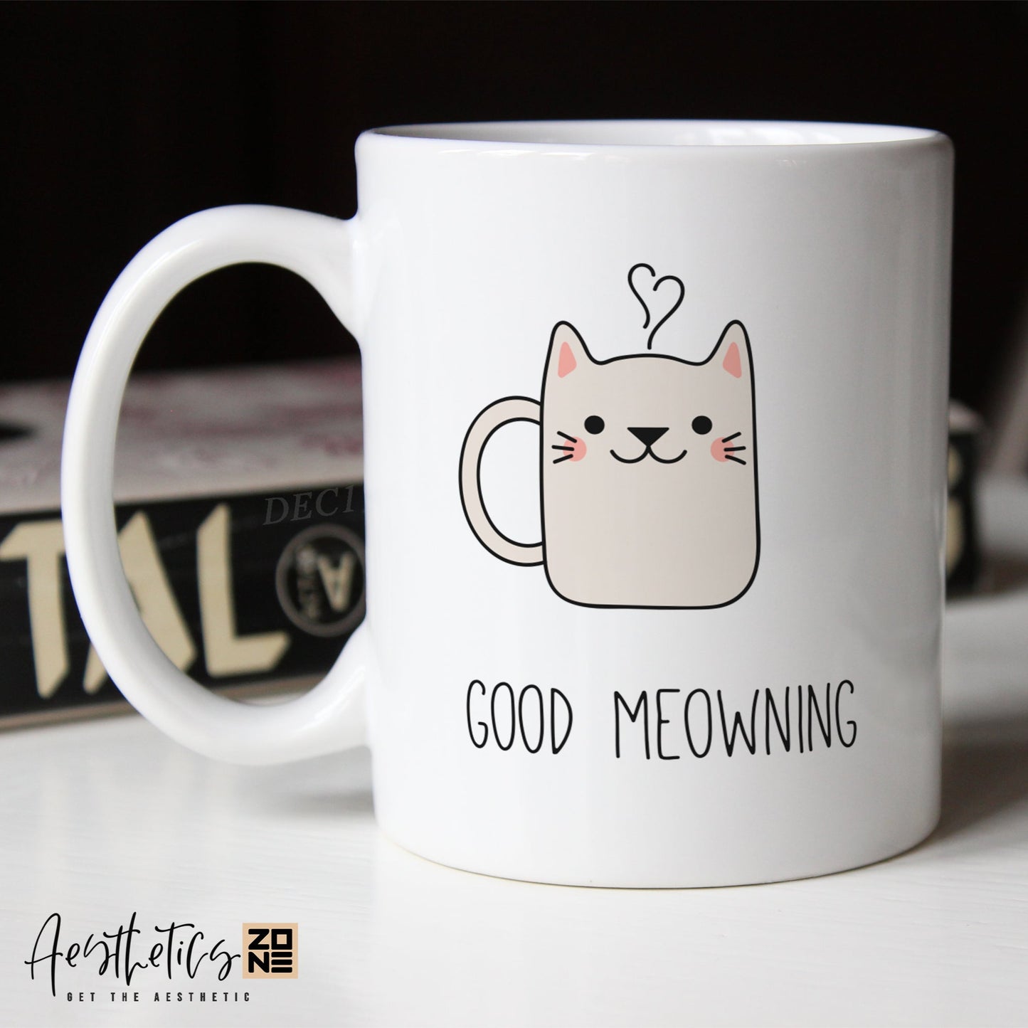 White coffee mug with a cat illustration and 'Good Meowing' text on a blurred background