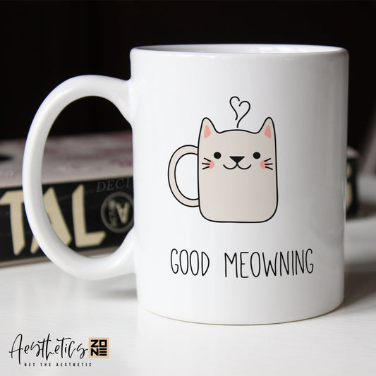 White coffee mug with a cat illustration and 'Good Meowing' text on a blurred background