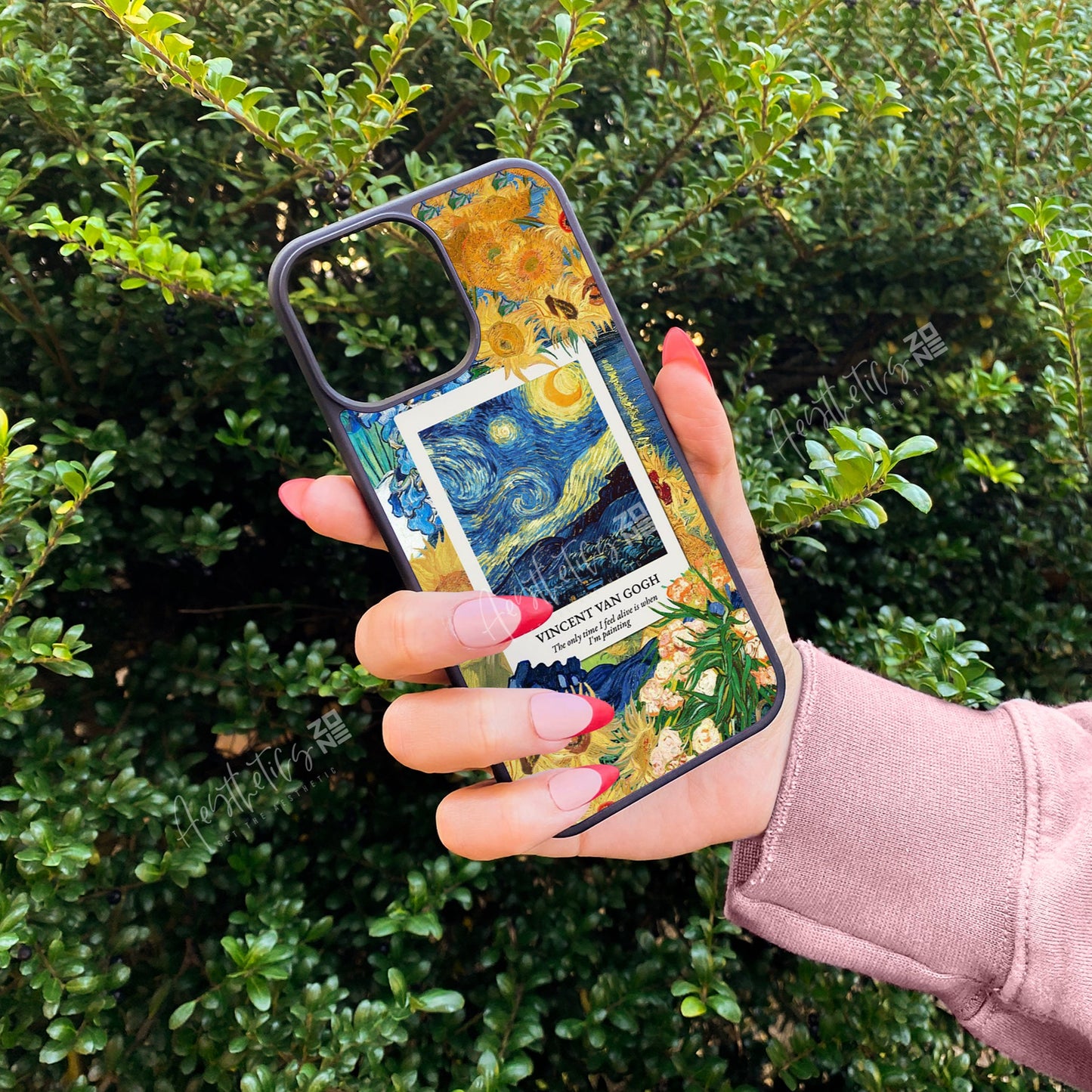 Person holding a phone case with artistic design in front of green bushes