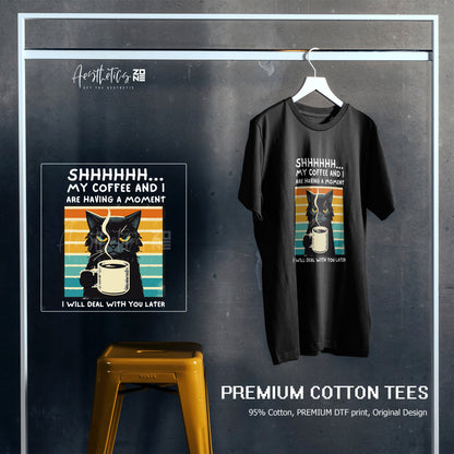 Black t-shirt with a graphic design of a cat and coffee cup, displayed on a hanger against a dark background.