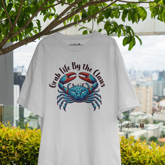 White t-shirt with a blue crab graphic and text, hanging outdoors with greenery and cityscape in the background.