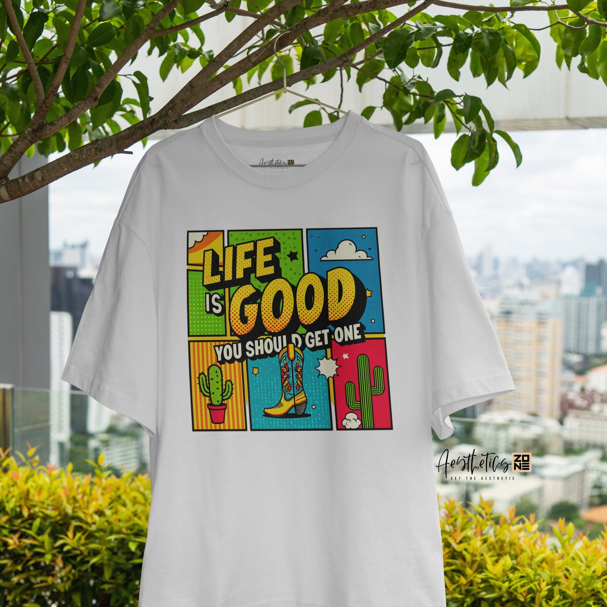 White t-shirt with colorful graphic design hanging outdoors with greenery and cityscape in the background