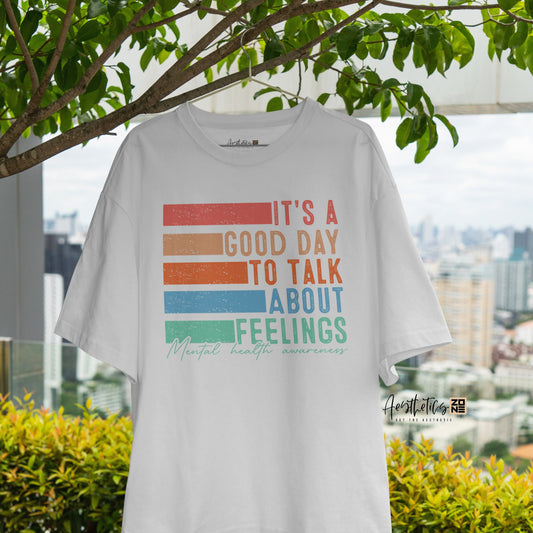 White t-shirt with colorful text design hanging outdoors with greenery and a cityscape in the background